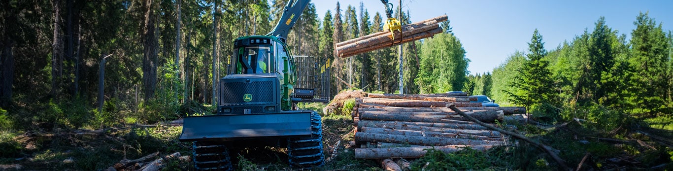 A John Deere Forwarder stacking logs in a forest.
