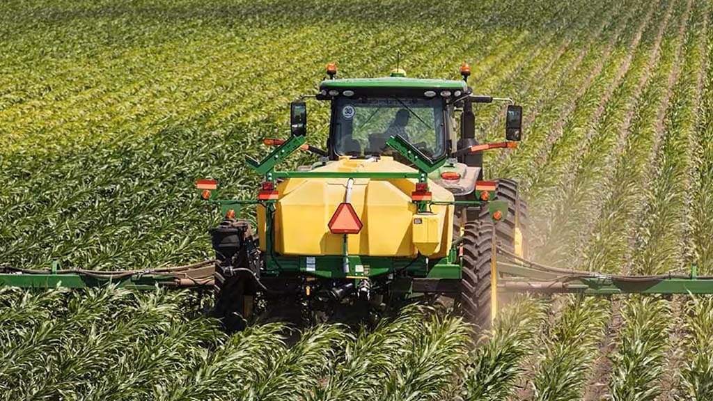 John Deere 2530L nutrient applicator is operating in a field, showcasing its long frame and multiple row units designed for liquid fertilizer application.