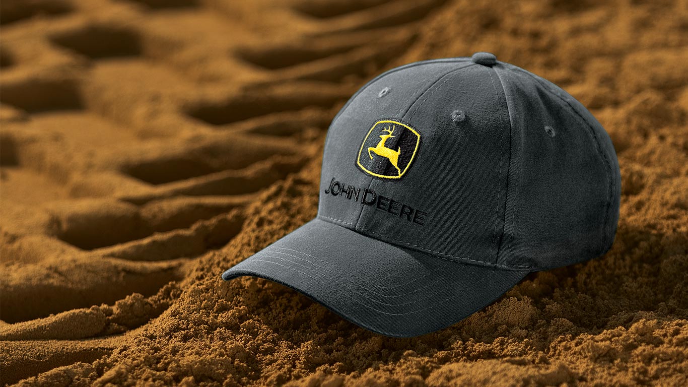 Gray John Deere cap resting on brown soil with deep tire tracks.