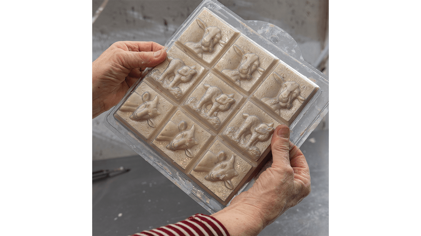 Hands holding a mold with twelve square tiles featuring raised horse designs.