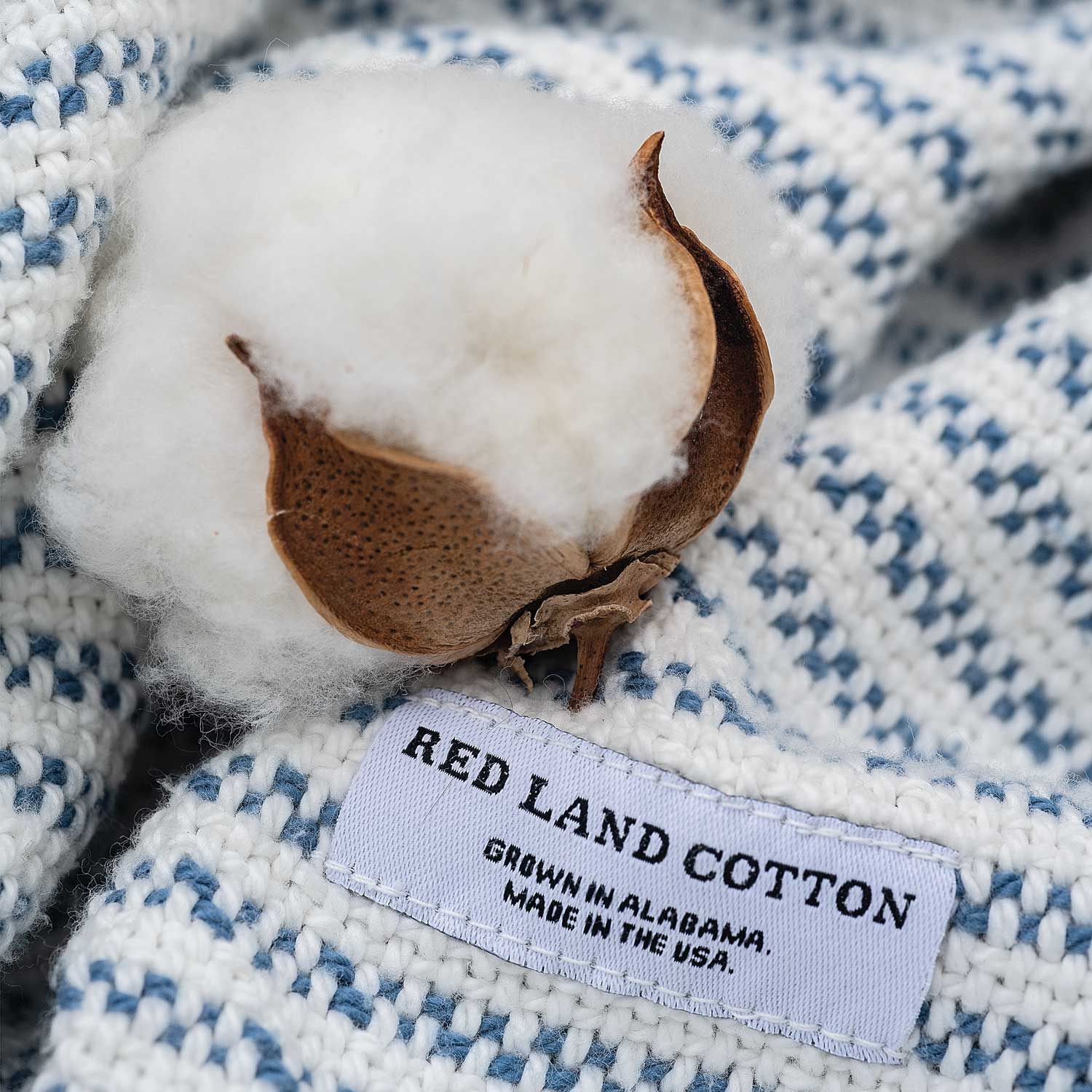Cotton boll on blue-and-white woven fabric with tag reading "Red Land Cotton, Made in USA."