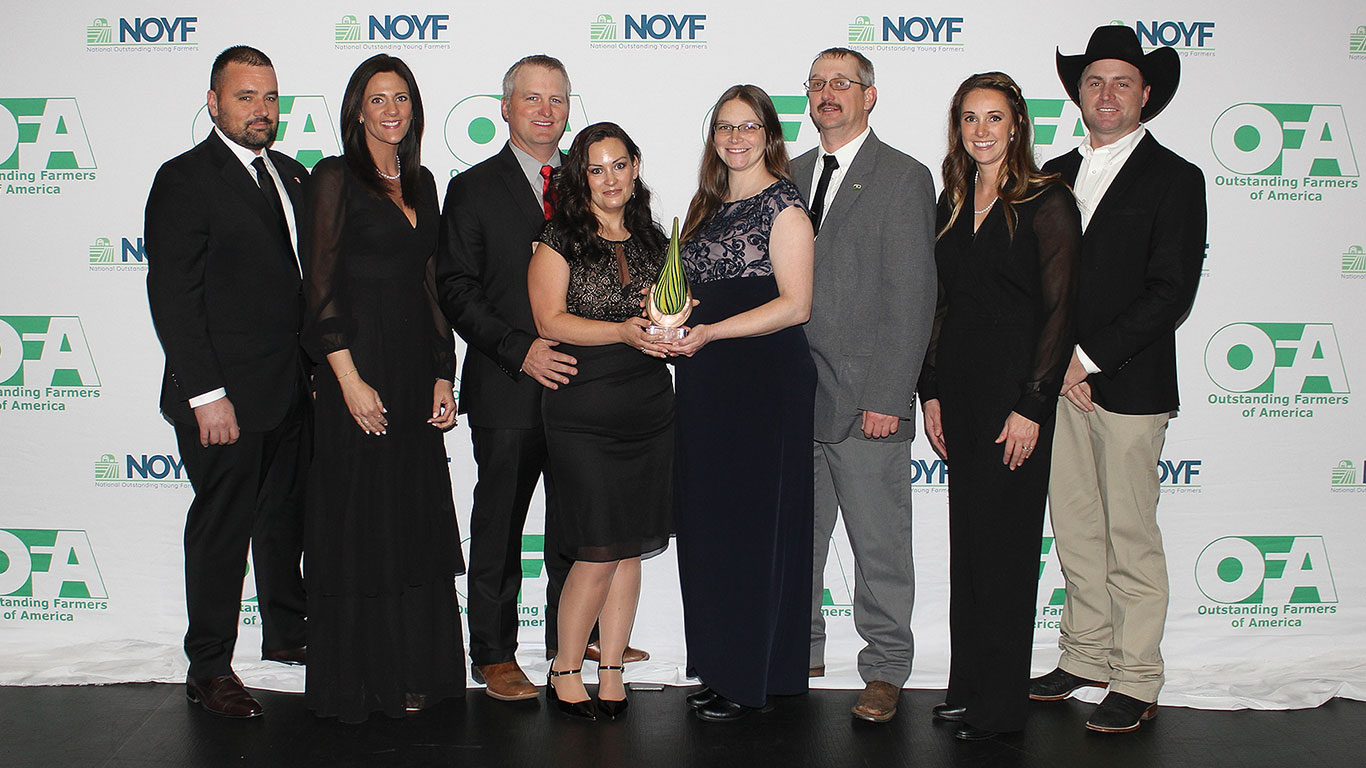 Eight people posing at event holding award; OFA logo backdrop