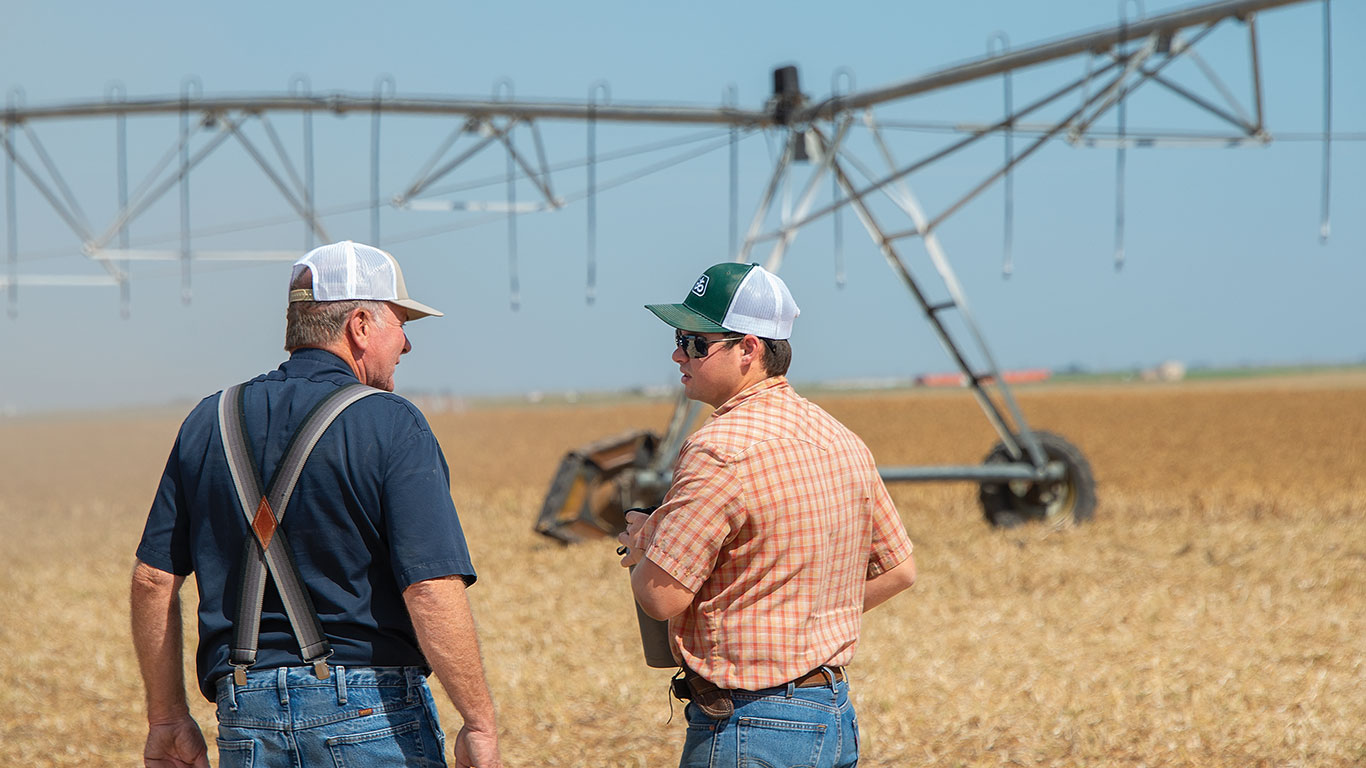 Two people talking near irrigation equipment on farmland