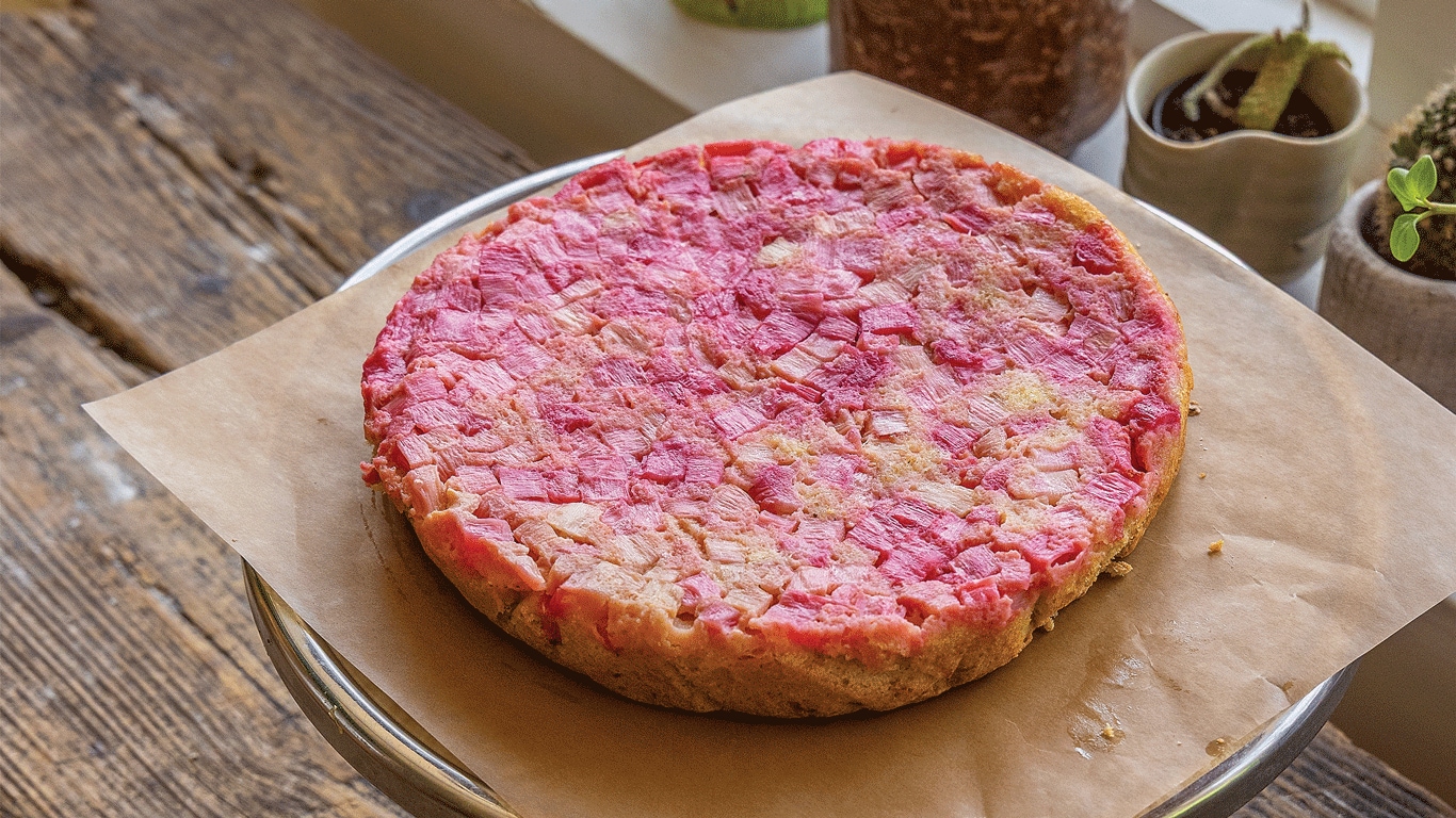 Pink dessert on parchment paper atop wooden table by window/plants