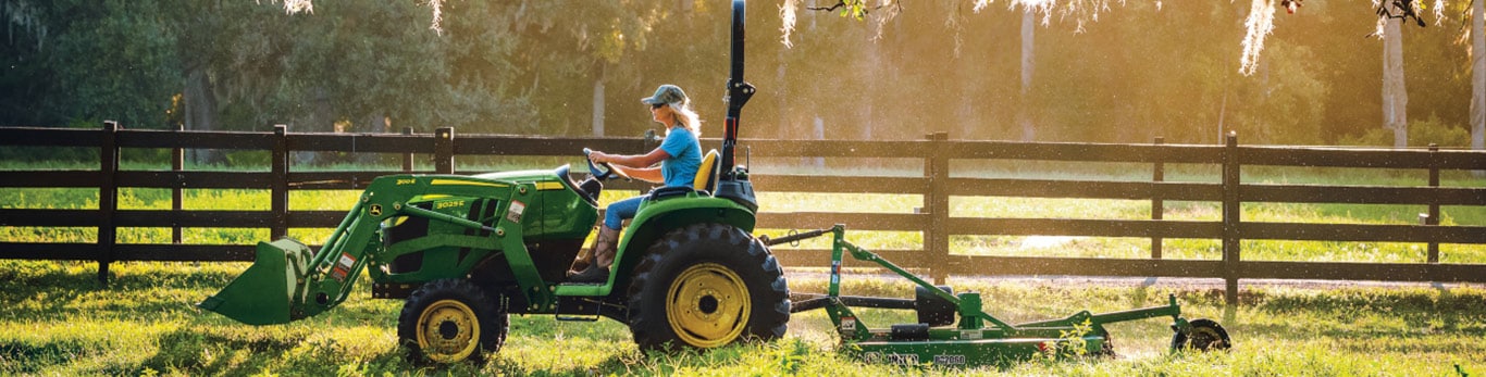 person driving a compact tractor equipped with a loader and a mower