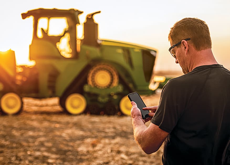 Person checking cell phone in the field to operate an autonomous tractor