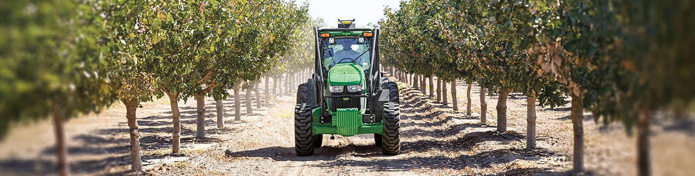 Green tractors moving through a row of trees.
