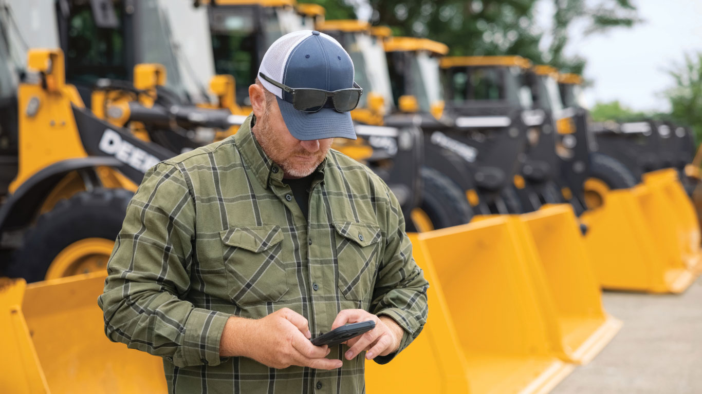 Customer using a mobile phone to make a John Deere Financial payment outdoors near equipment.