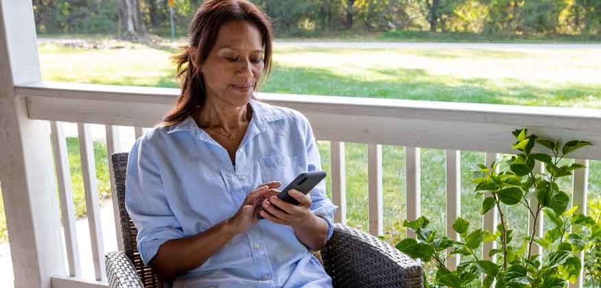 Woman sitting on a chair on her porch looking at her cell phone