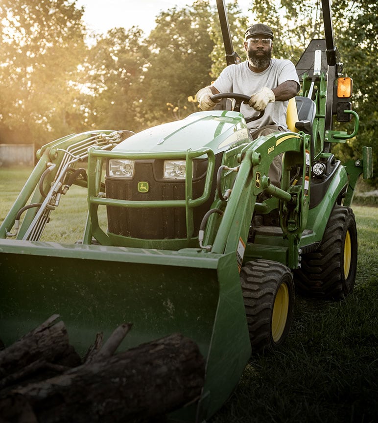 A man hauls wood logs on a 1025R Compact Utility Tractor