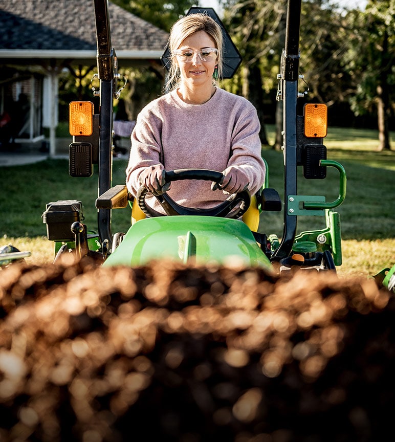 A woman hauls dirt on a John Deere 1025R Compact Utility Tractor