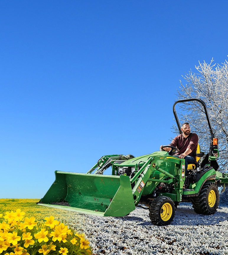 A man driving a John Deere 1025R Compact Tractor with Loader attachment from snow-covered grass to blooming fields.