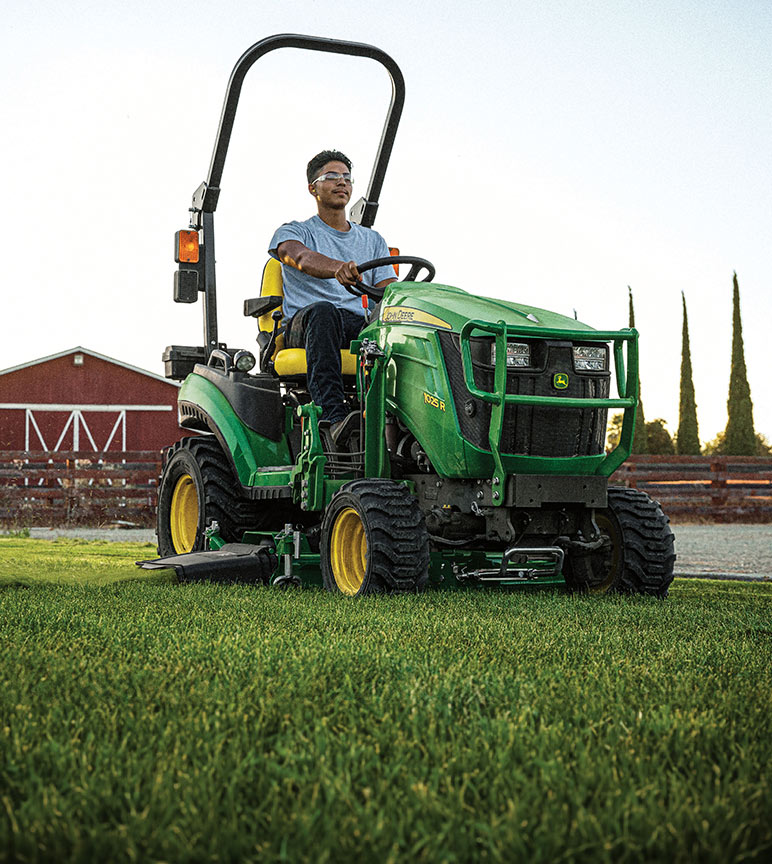 Man operating a 1025R tractor in front of a red barn