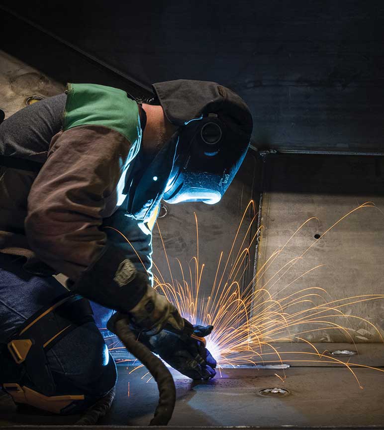 A person in welding suit welding a piece of equipment with sparks flying