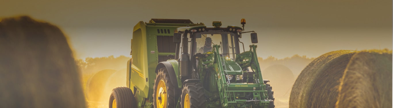 6120M Tractor with a 461M Round Baler bales hay at sunset