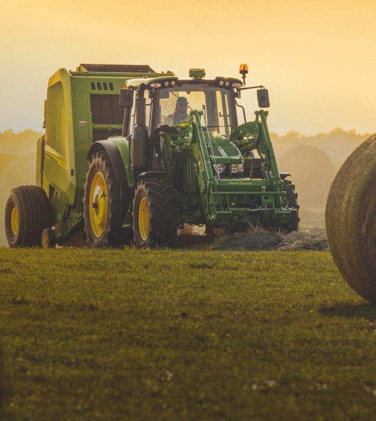 6120M Tractor with a 461M Round Baler bales hay at sunset