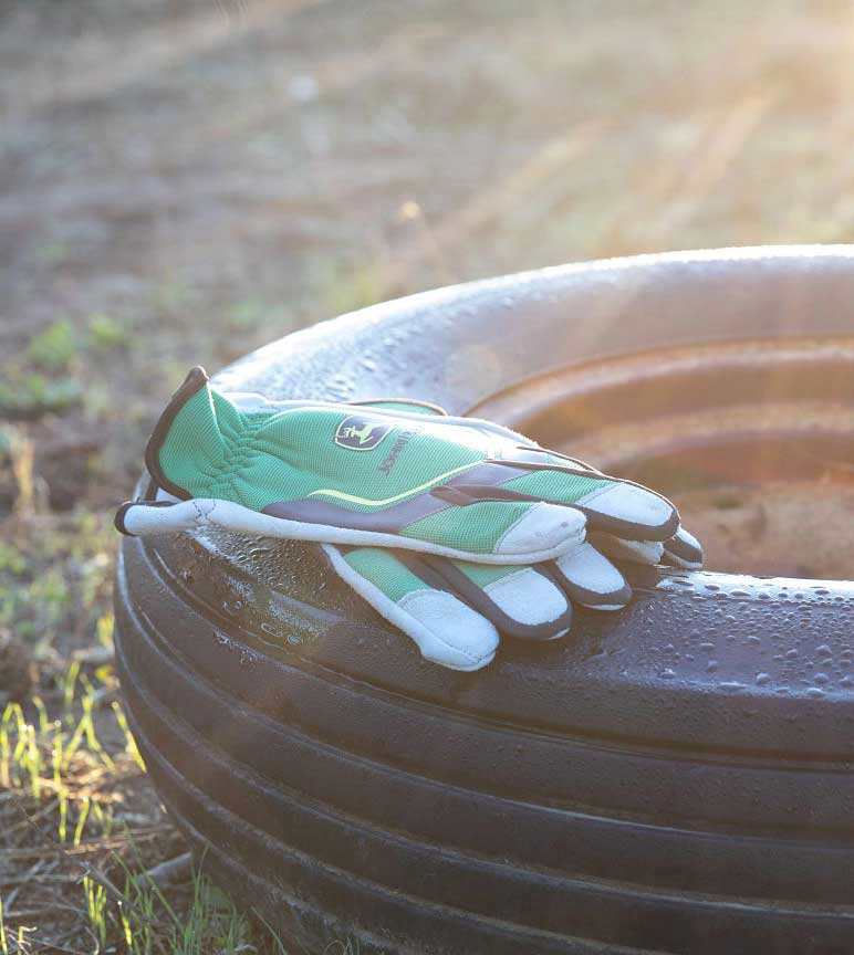 John Deere work gloves on a tire in a hay field