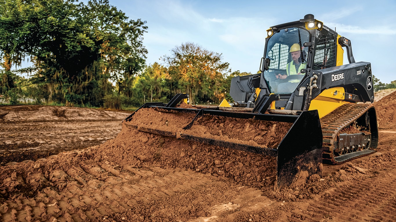 333P Compact Track loader pushes dirt with a box blade attachment in a field