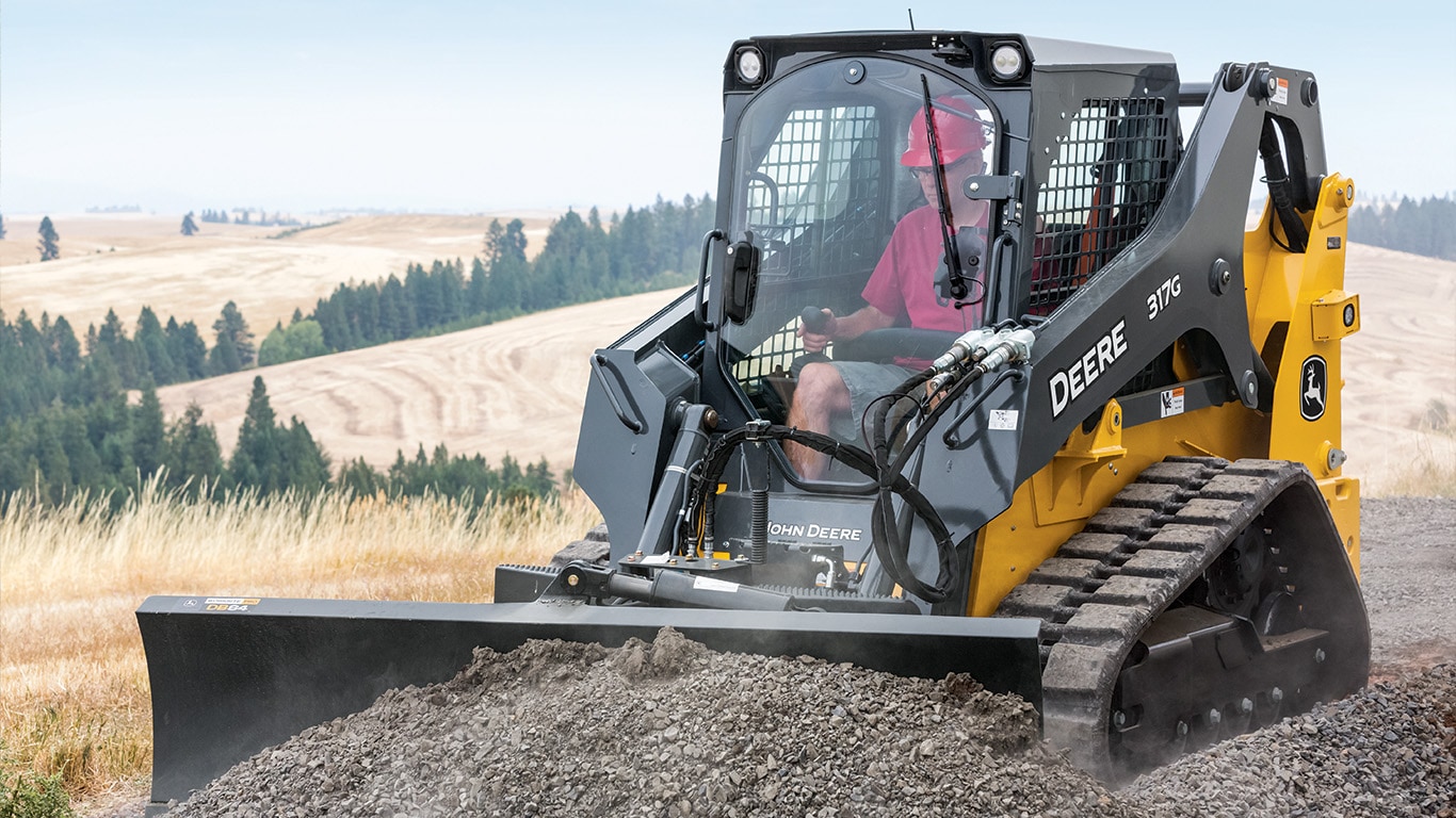 a 317G uses dozer blade to push gravel in a field