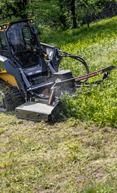 a 333 P-Tier CTL with an RX 84 Rotary Cutter is cutting tall grass by a treeline