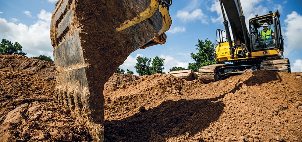 A John Deere 350 P-Tier SmartGrade Excavator backfills dirt into the trench of a completed stormwater pipeline at a site development.