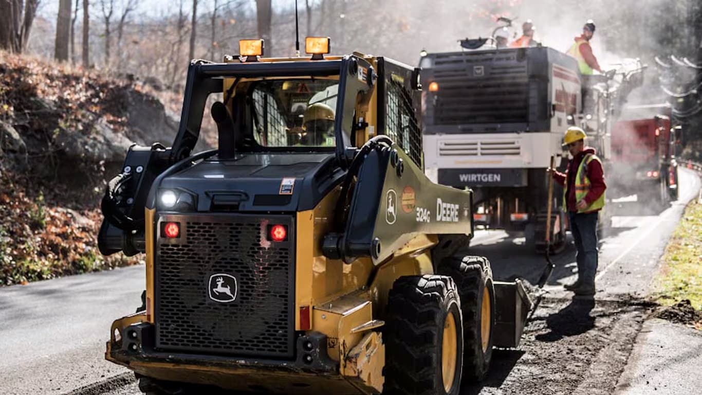 A man standing next to a 324G and Wirtgen Compact Milling Machine doing road construction