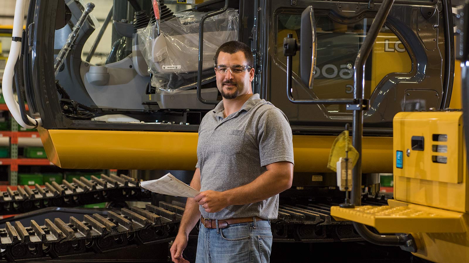 Jacob Henderson, un ingegnere di progettazione del processo di sviluppo del prodotto, mostrato mentre lavora nella fabbrica Deere-Hitachi davanti a un escavatore John Deere