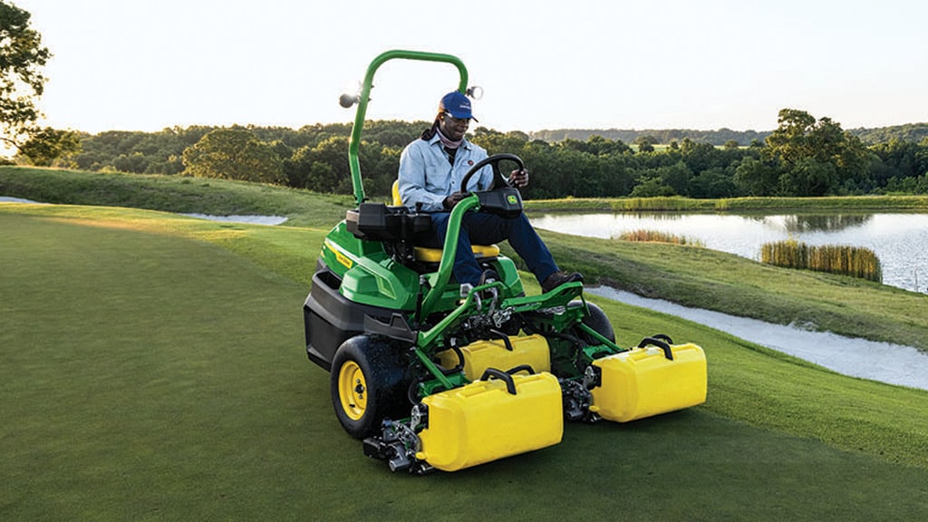 A person driving a mower along gold course