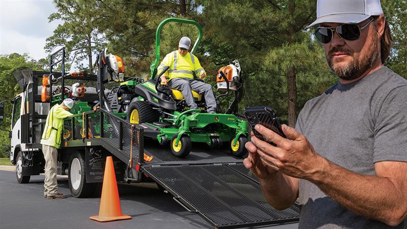 Man looking at his phone while his teammates load mowing equipment onto trailer.