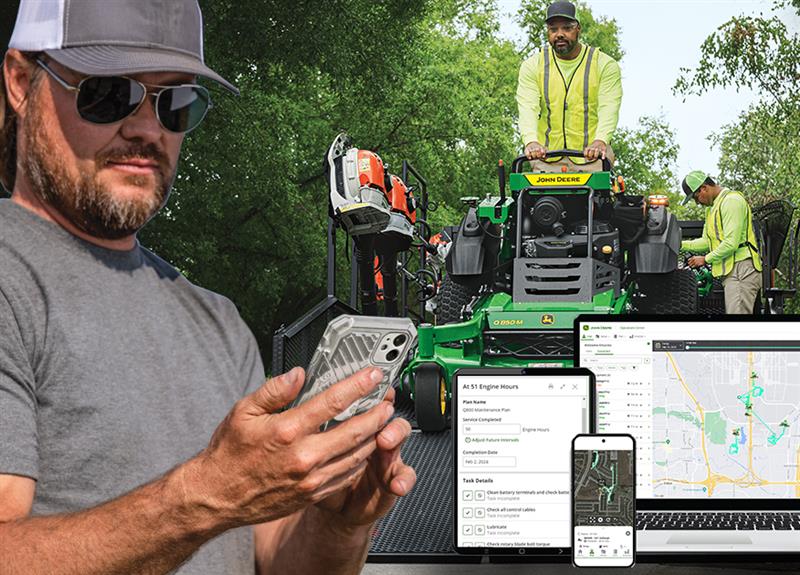 A person views a phone as a worker drives a stand-on mower off of a trailer; off to the side are Operation Center displays.