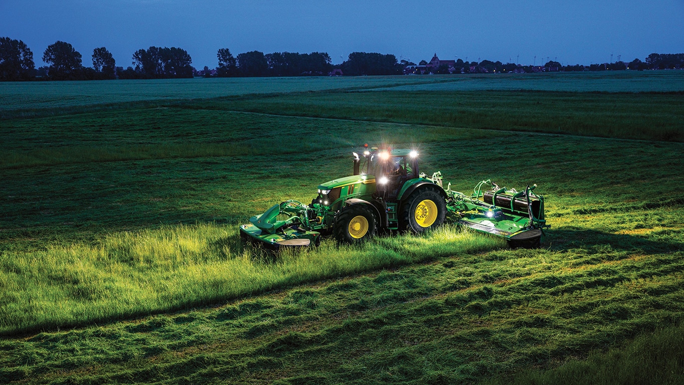 6M Tractor with F310R and R930R Mower Conditioners cutting hay in a field at night with tractor lights on for visibility