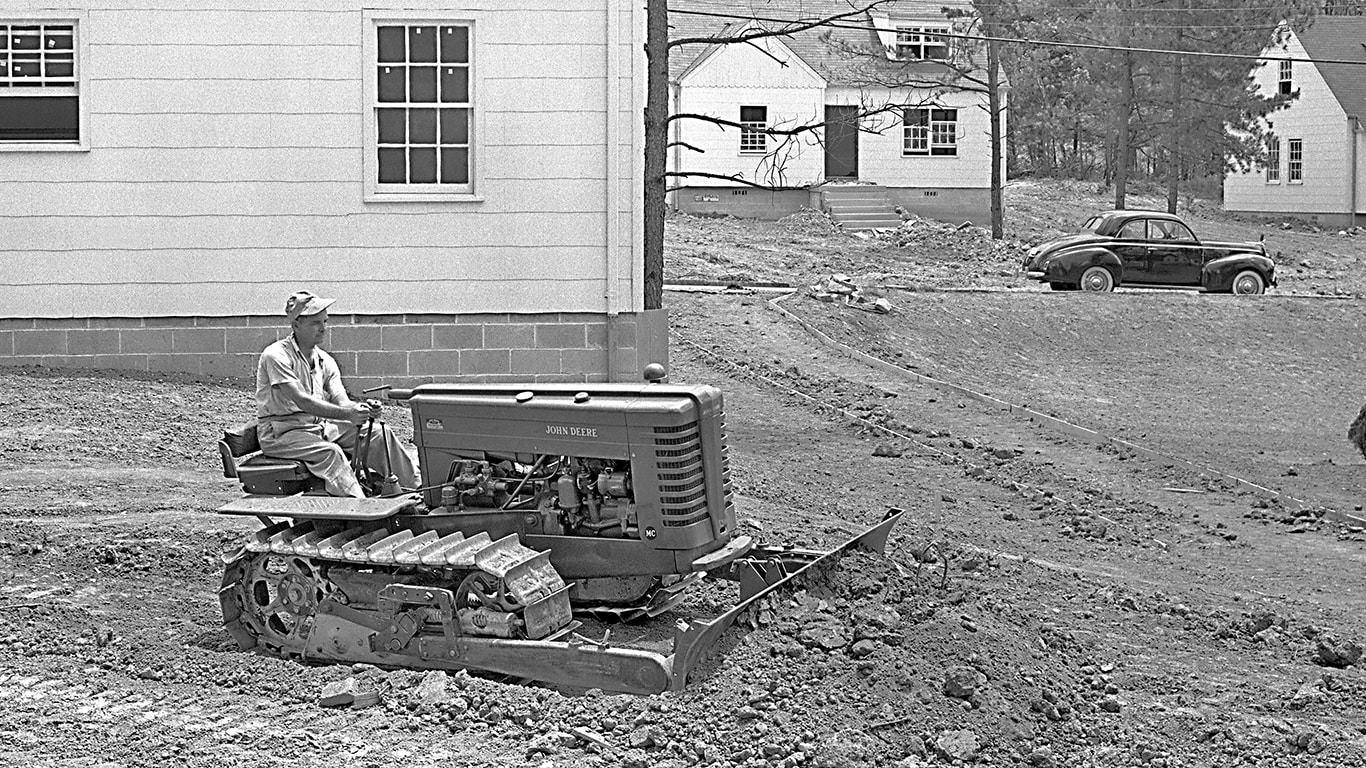 Vintage black and white image of a John&nbsp;Deere dozer pushing dirt in front of a building