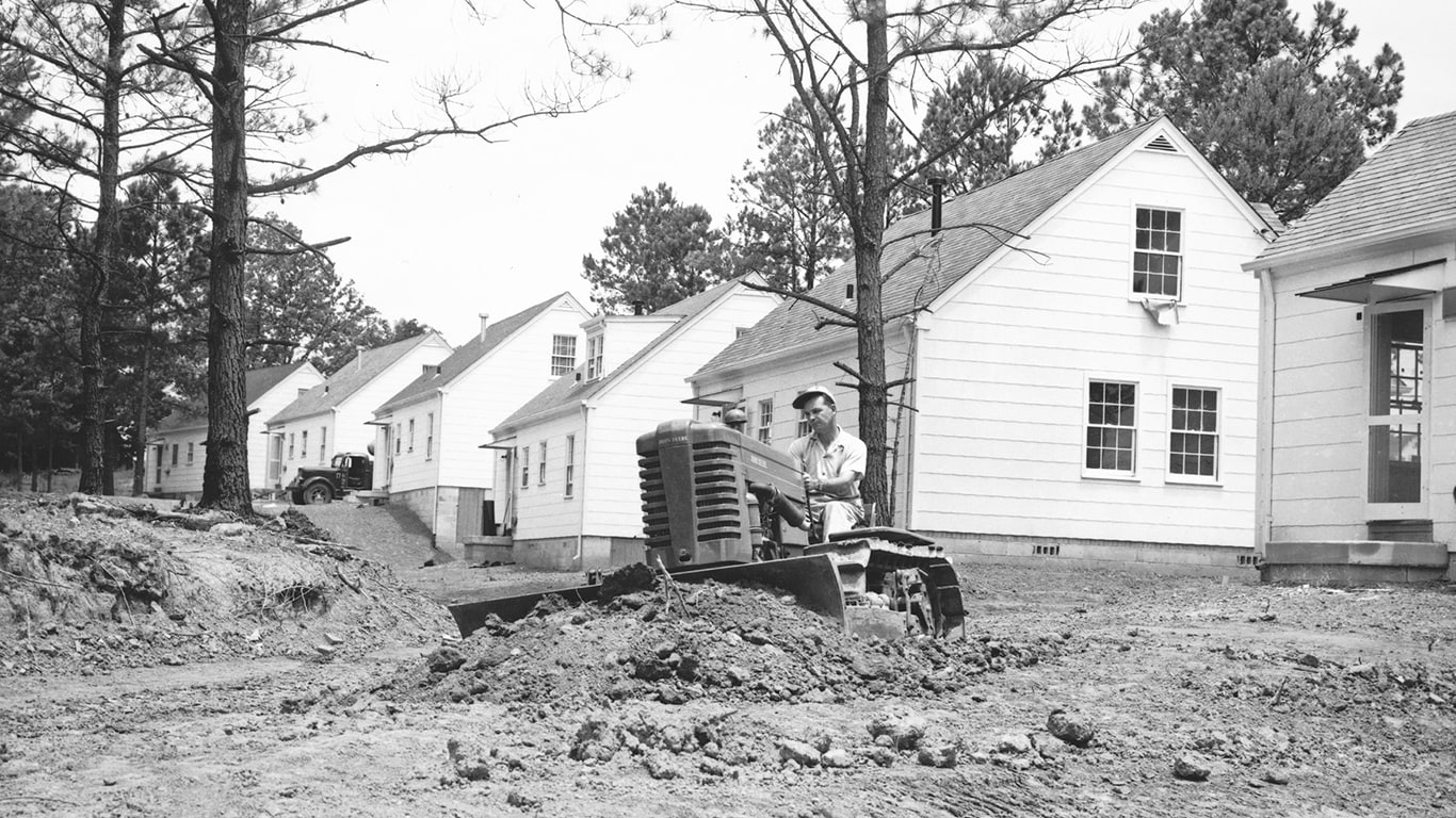 Vintage black and white image of a John&nbsp;Deere Dozer in front of a neighborhood