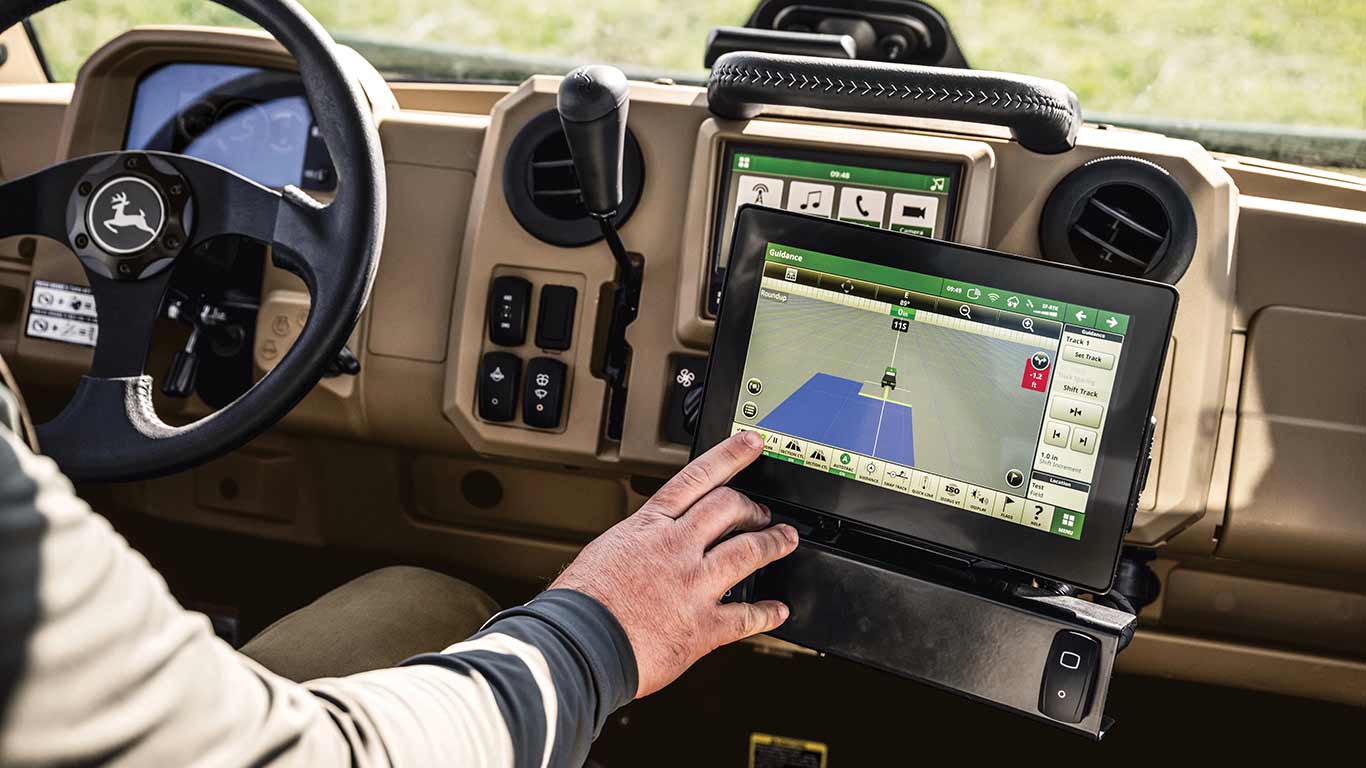 Operator sitting behind the wheel of a new John Deere Gator XUV 845R Signature Series Utility Vehicle using his index finger to interact with the touchscreen of the GS display as the screen shows the Gator's position in the field