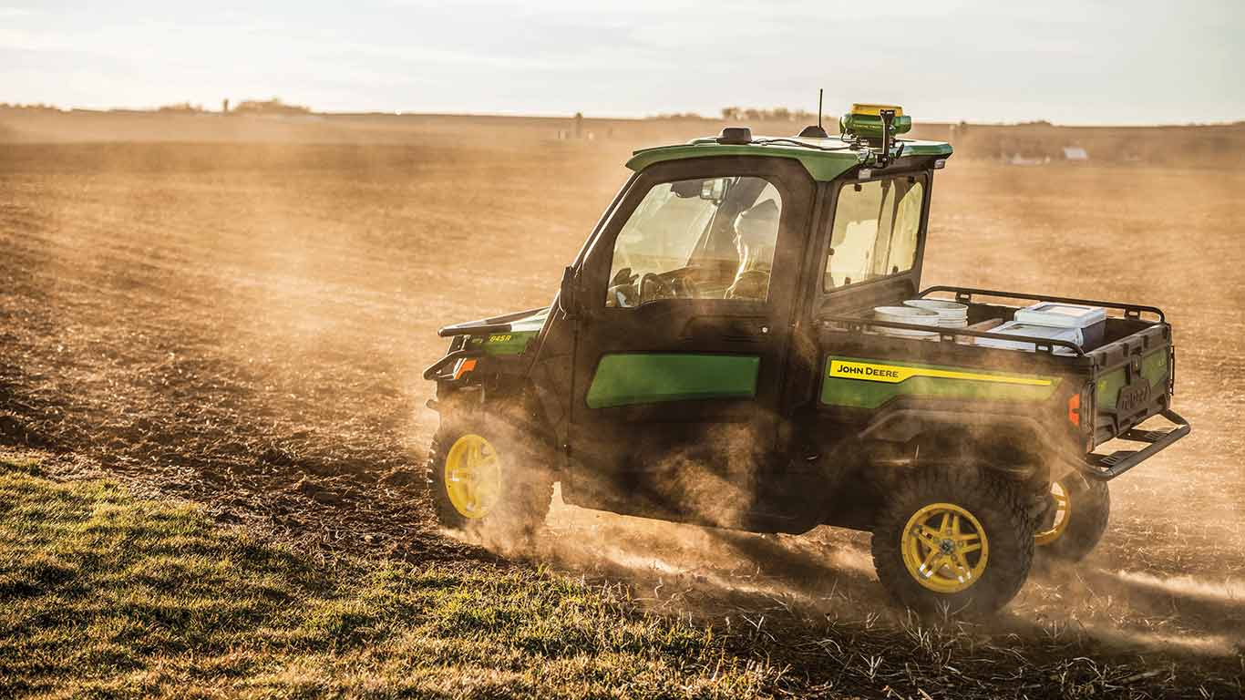 New John Deere Gator XUV 845R Signature Series Utility Vehicle with StarFire receiver moving through a field with dust swirling with a golden sunset look to the photo