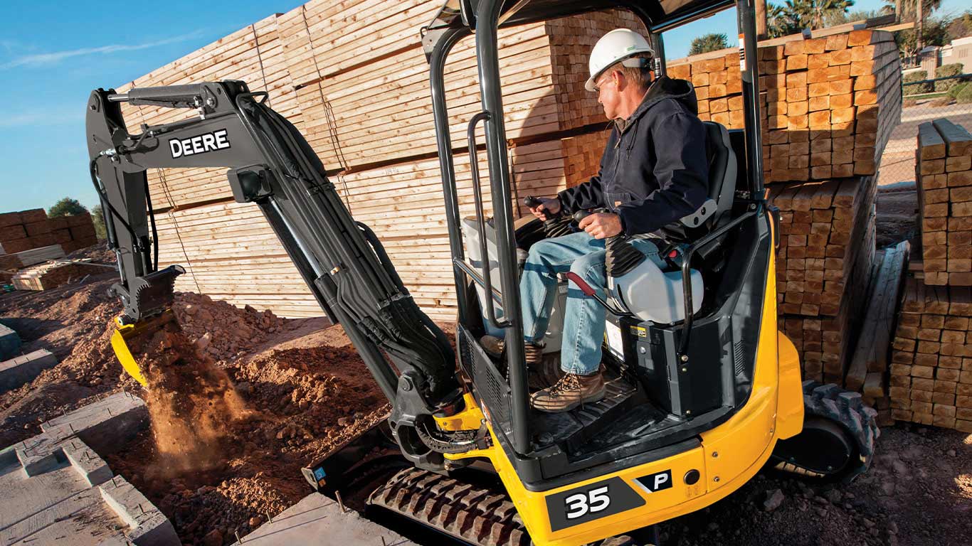 Operator using a John Deere 36 P-Tier Mini Excavator to unload a bucket of dirt at a construction site