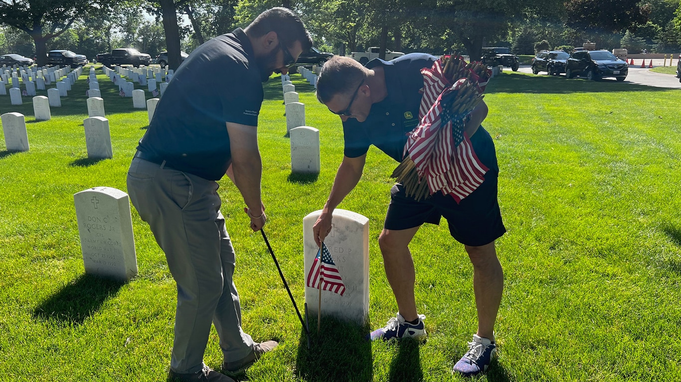 Two people placing a United States flag on a veteran's grave
