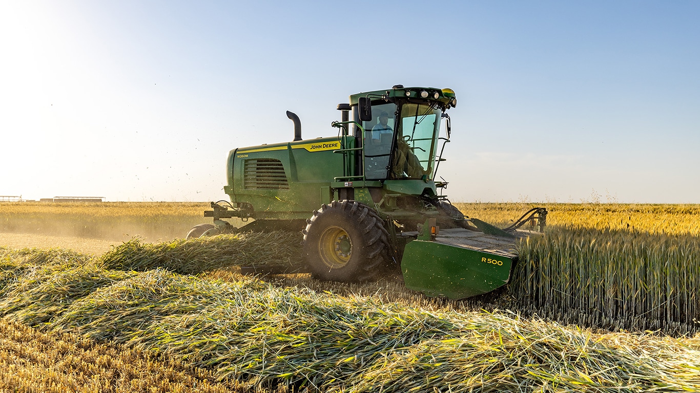 Side view of the new Self-Propelled Windrower M Series, W260M model, as part of the John&nbsp;Deere Hay and Forage Equipment portfolio, with a Header Windrower Platform R500 Attachment, together cutting a triticale mix with the sun shining down on a field in Tulare, California.