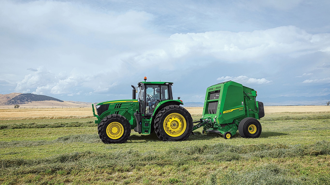 John&nbsp;Deere 6R Series Tractor pulling a John&nbsp;Deere 1 Series Round Baler in a hay field with windrows on either side of the tractor-baler set-up.