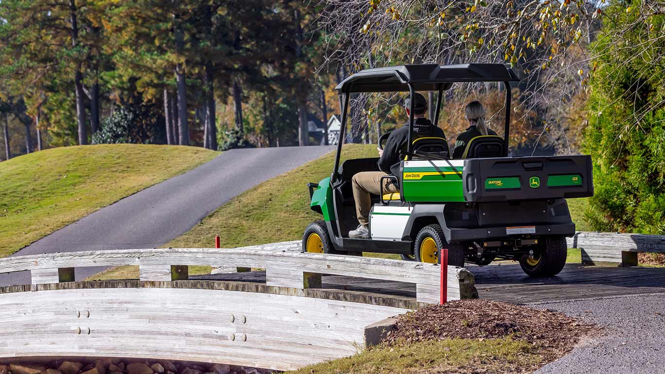 Back view of a man and woman riding in electric gator while going over a bridge.