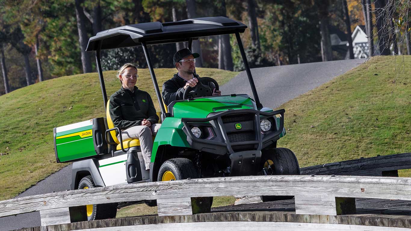 Front view of a man and woman riding in electric gator while going over a bridge.