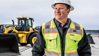 A person in a hardhat walks in front of a fleet of wheel loaders