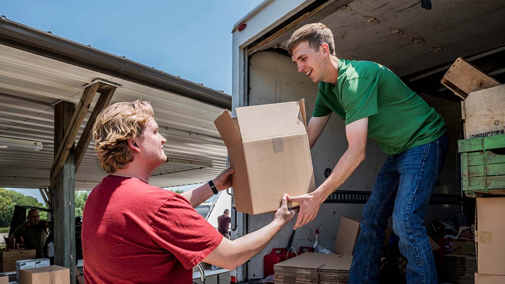 Person handing another person a box and loading it in a truck