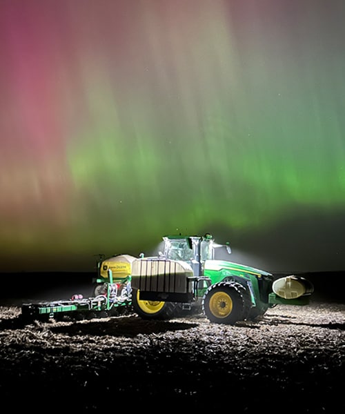 A John Deere tractor and a colorful Northern Lights night sky