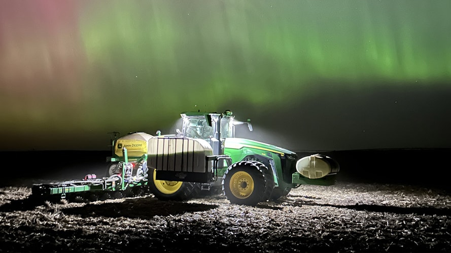 John Deere tractor under a colorful Northern Lights night sky.