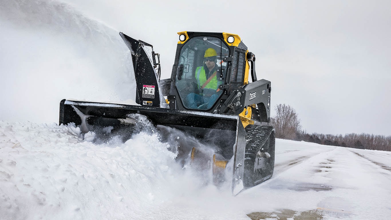 Compact track loader with snow blower attachment clearing snow.