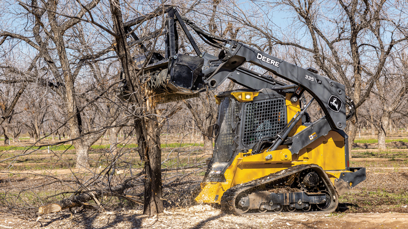 335 P-Tier compact track loader using mulching head to cut down trees in wooded area.