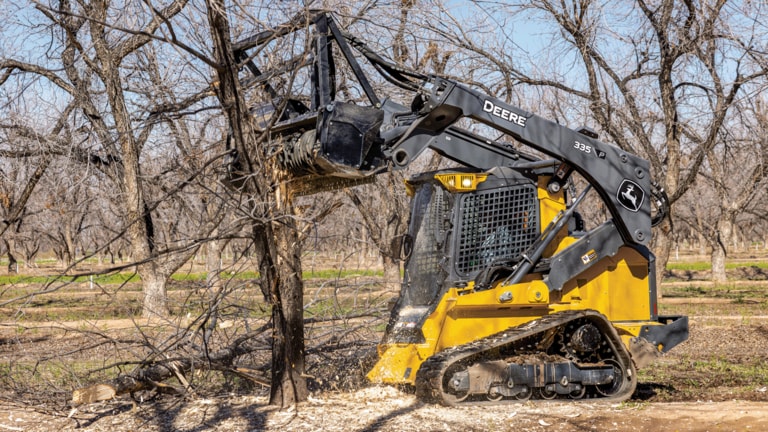 335 P-Tier compact track loader using mulching head to cut down trees in wooded area.