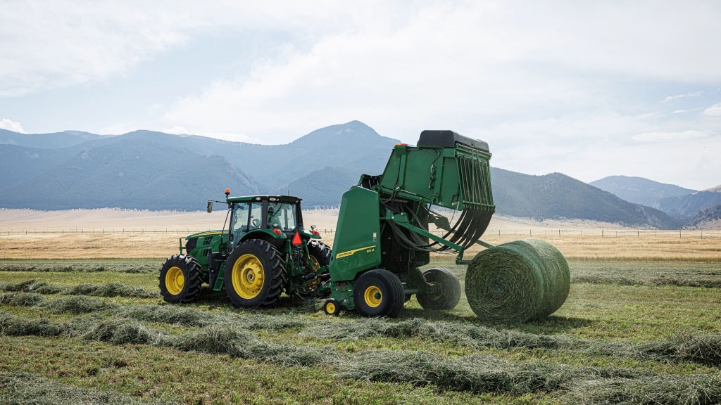 A tractor operating a 1 Series Round Baler while baling hay in a field