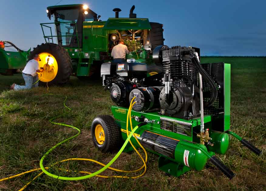 two people working on a John Deere tractor in a field using an air compressor